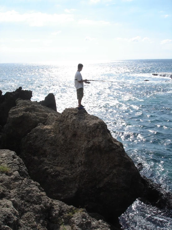 a man standing on the rock at the edge of the ocean