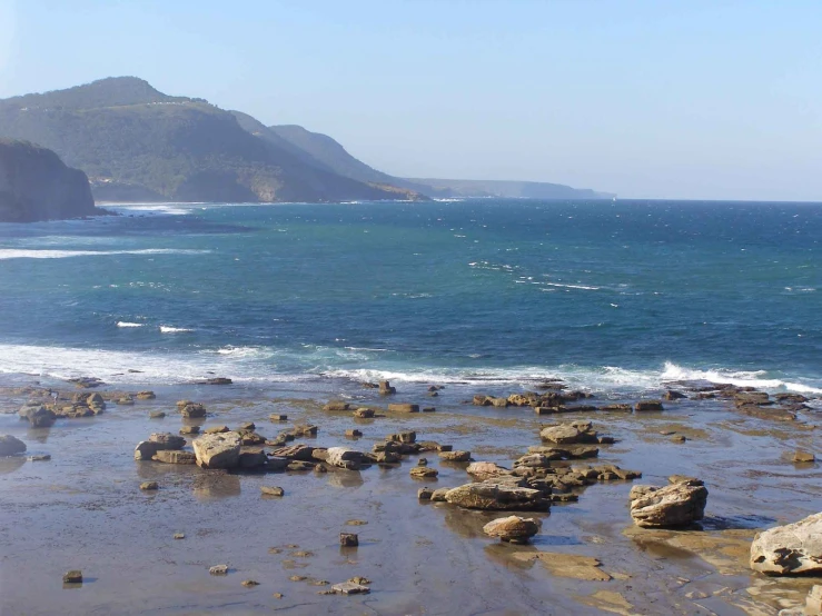 the beach has many rocks along it and is near a mountain