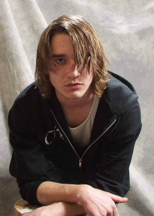 a young man leaning on a stool wearing a jacket