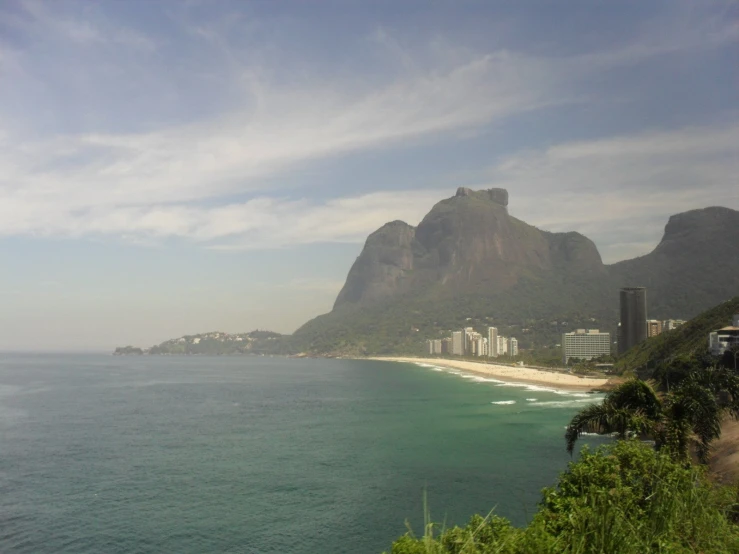 a beach with lush vegetation, mountains and buildings