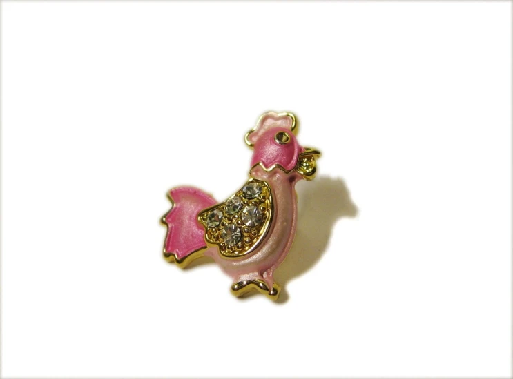 a pink and gold brooch with a brown bird sitting on it