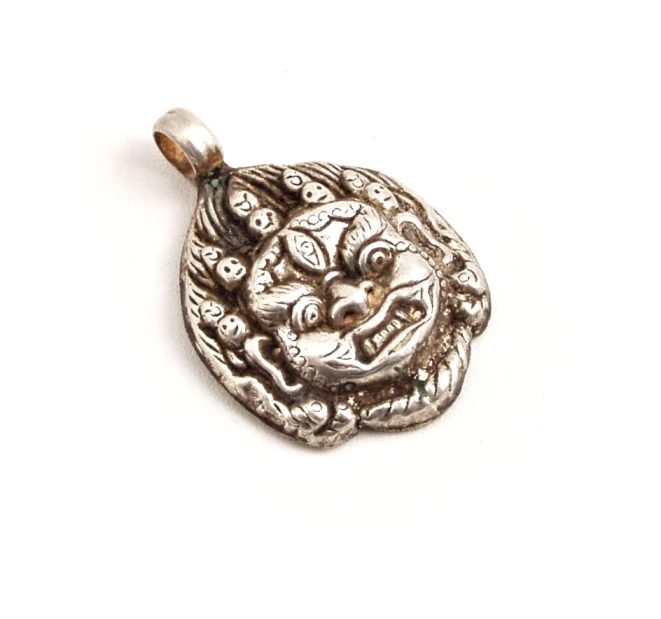 a silver pendant is sitting on a white surface