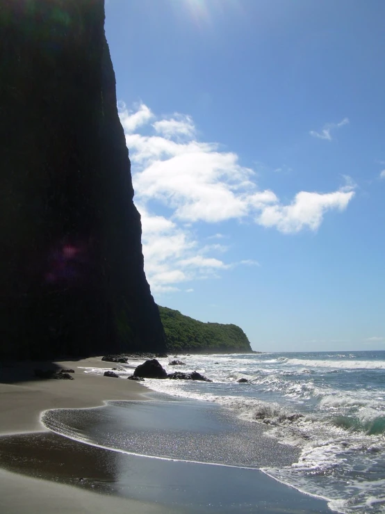 the shore line and rocky cliff are viewed from the sandy beach