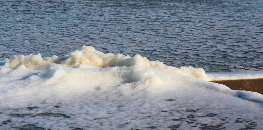 small wave on shore, with boat sailing in background