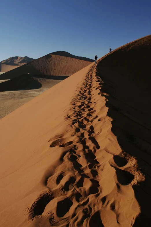 two people hiking uphill on a very tall sand dune