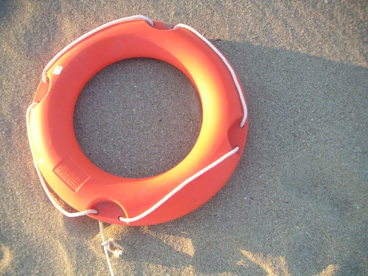 an orange lifebuoy is on the sand near the water