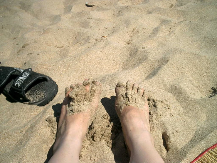 this is a persons feet in the sand with a pair of shoes near by