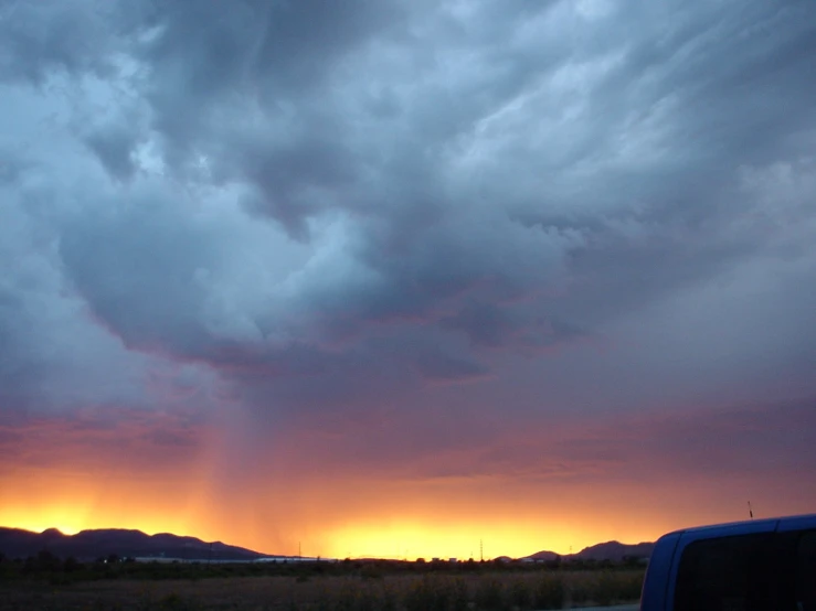 the sunset behind some clouds over a grass field