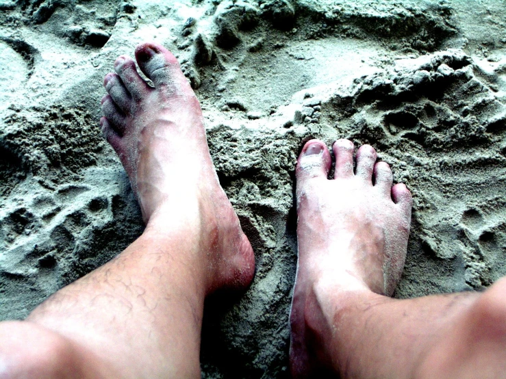 a person standing in the sand while their feet are sticking out