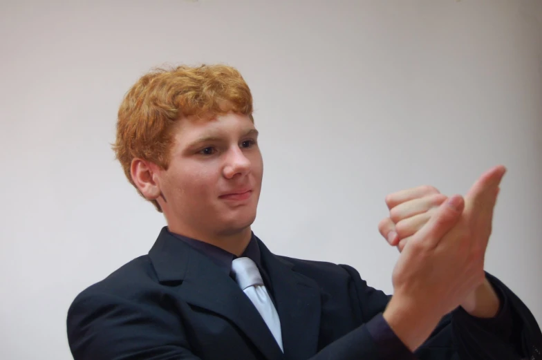 a young man in a suit sitting down giving a peace sign