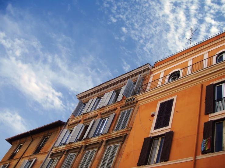 orange apartment building with white shutters and cloudy sky