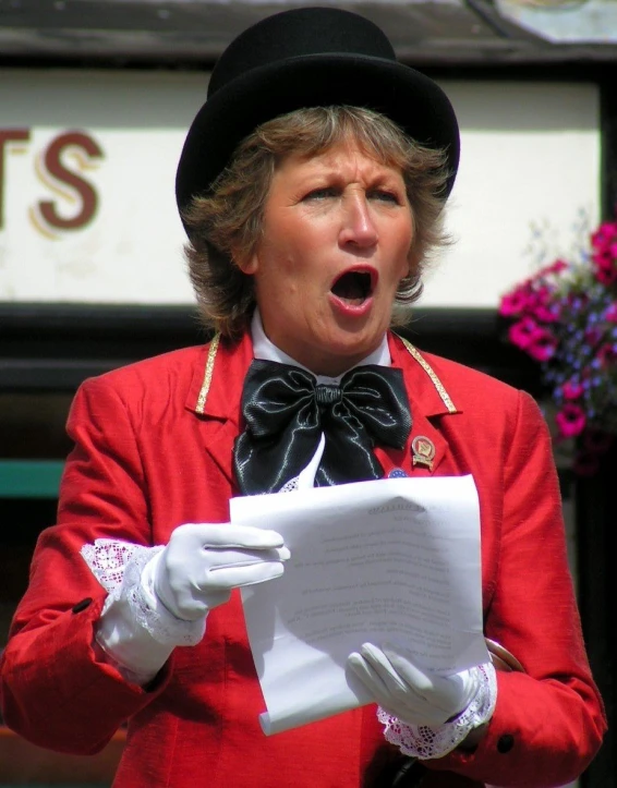 a woman in a black top hat sings while holding a piece of paper