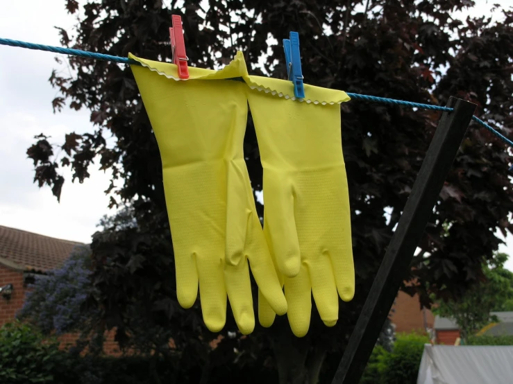 three oven mitts hanging from clothesline with house in background