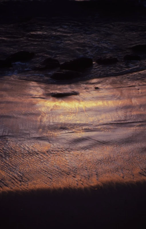 the sun sets over a rocky beach with foamy waves