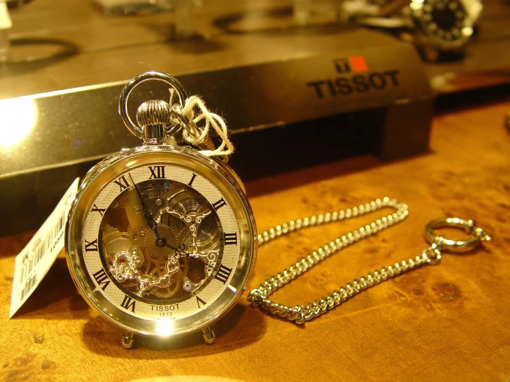 a pocket watch with a label on it sits next to a chain