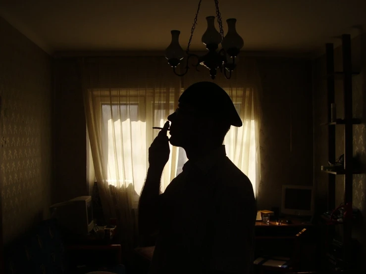 a man in the dark smoking a cigarette with a light shining on him