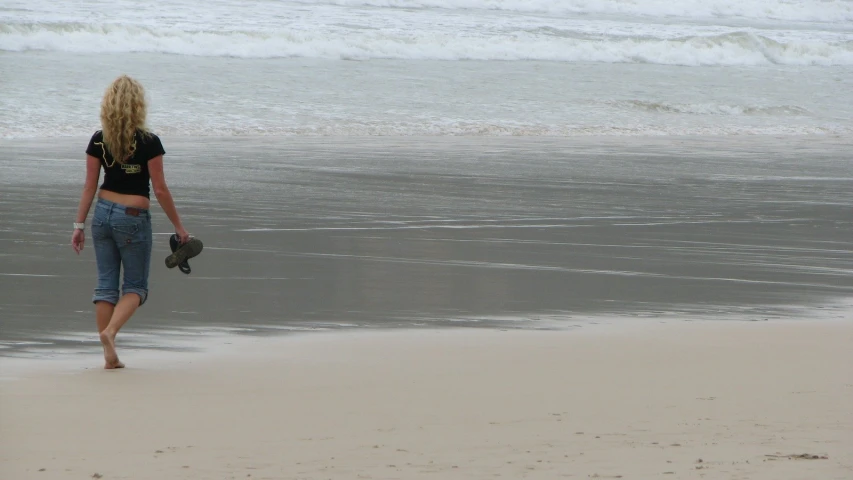 woman walking on the beach with hat in her hands