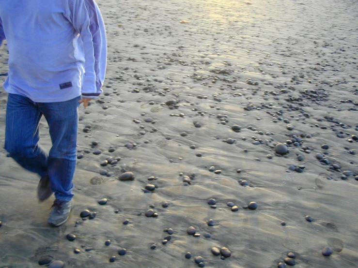 a man walking across a beach next to a body of water