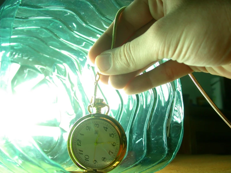 a clock hanging on the chain between a glass jar