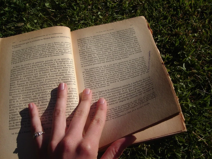 a hand holding onto an open book on grass