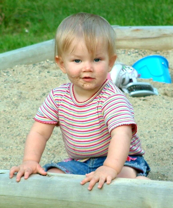 small child sitting on a sandbox looking at camera