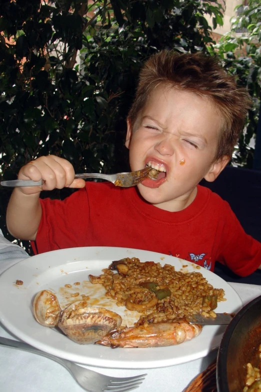 a boy eating from a white plate with vegetables