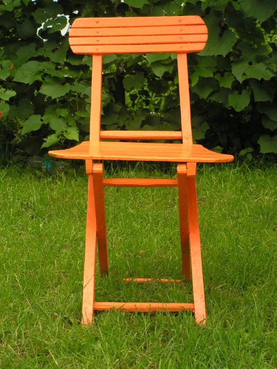 an orange chair stands upright on a green grass lawn