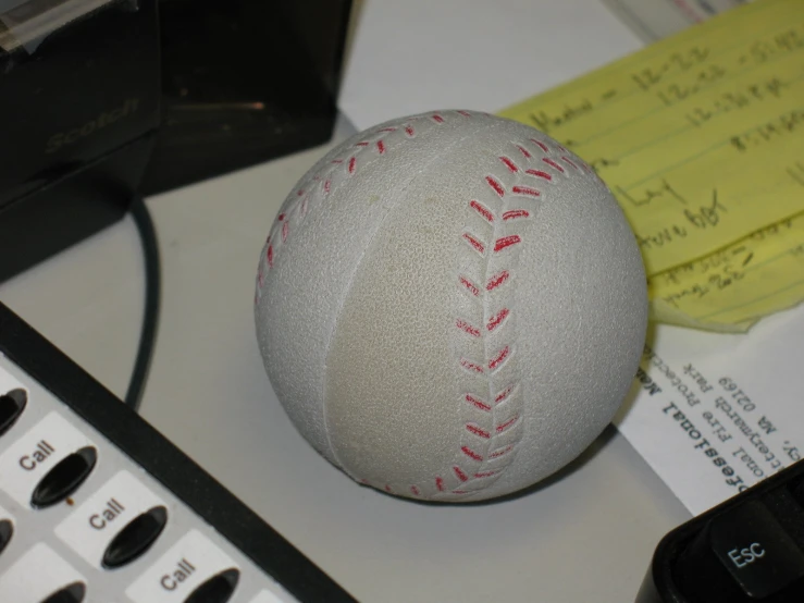 the baseball is resting on a desk next to a calculator