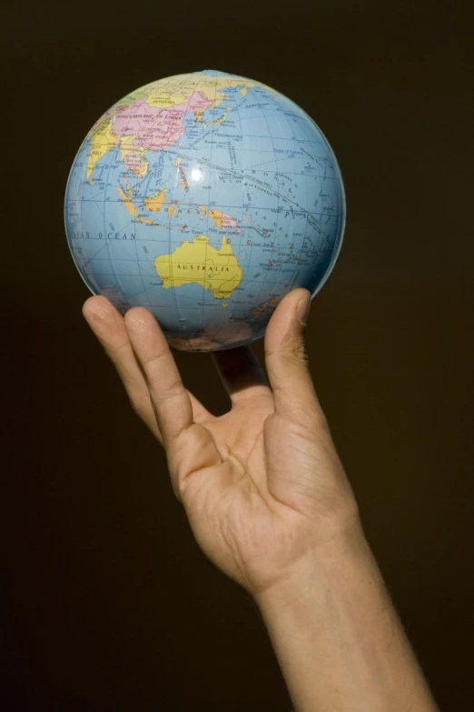 a hand holding up a blue and yellow terrestrial earth globe