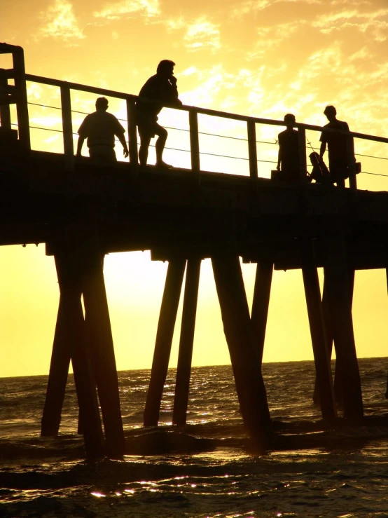 people walking on the pier at the ocean during a beautiful sunset