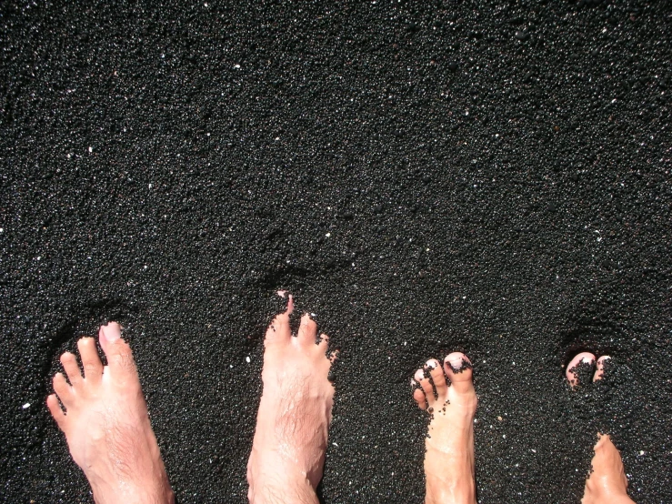 the four people are standing in a row on the black sand