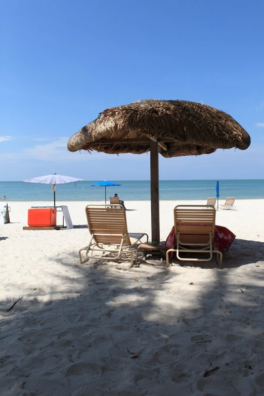 two lounge chairs sitting under a straw umbrella on the beach