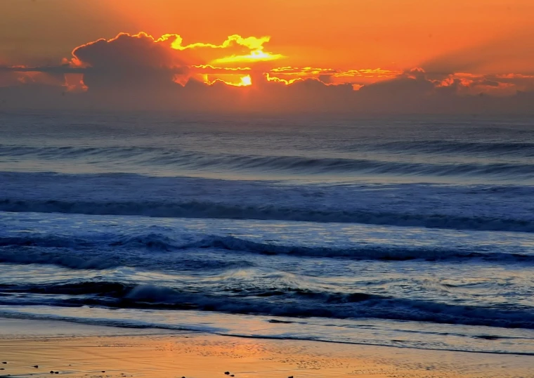 the sun set in front of a cloudy sunset at the beach