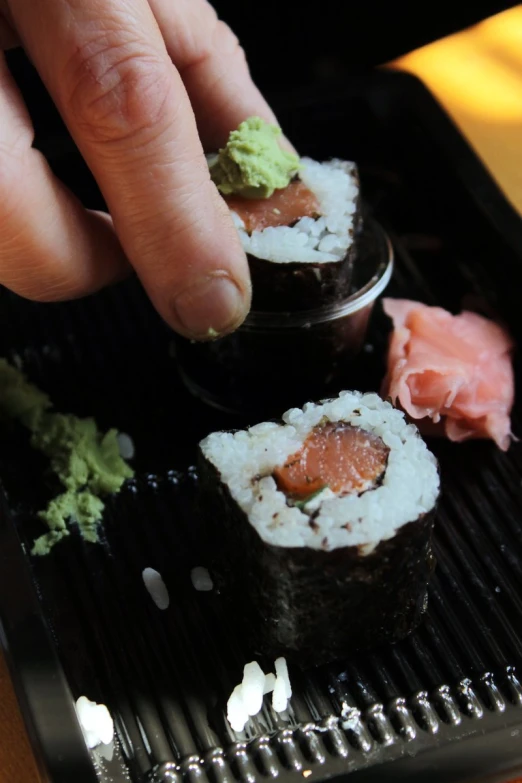 there is a hand grabbing two sushis out of the tray