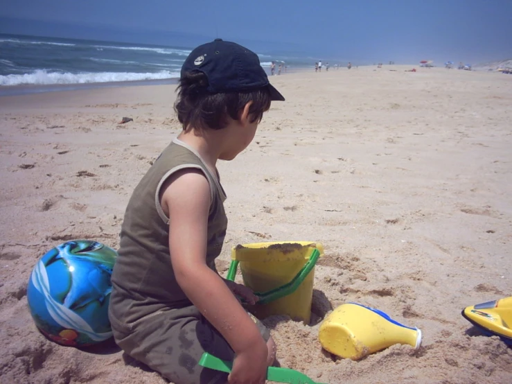 a little boy in a hat sitting in the sand on a beach