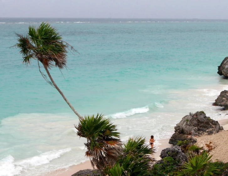 a boy walking into the ocean next to a large rock