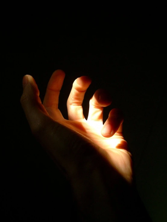a hand outstretched towards a spot light in the dark