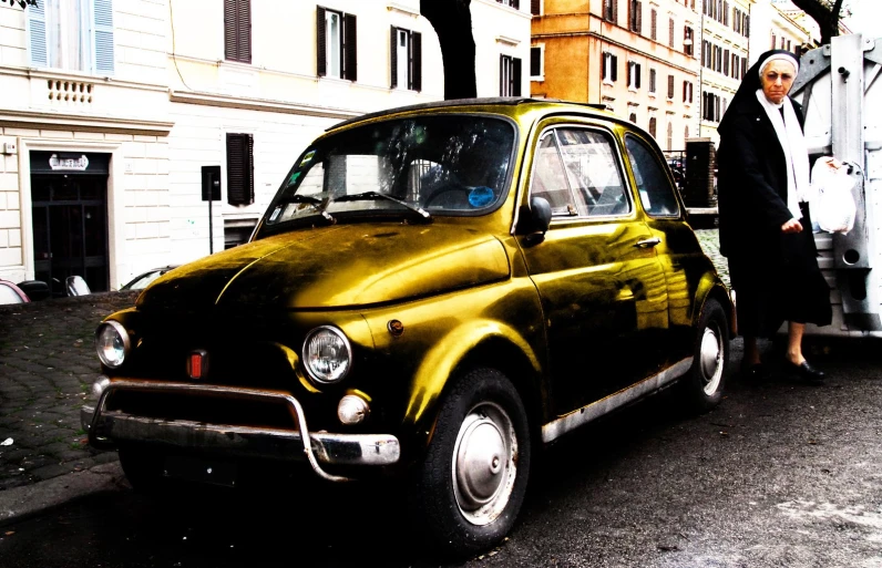 a man and woman stand next to an old style yellow car