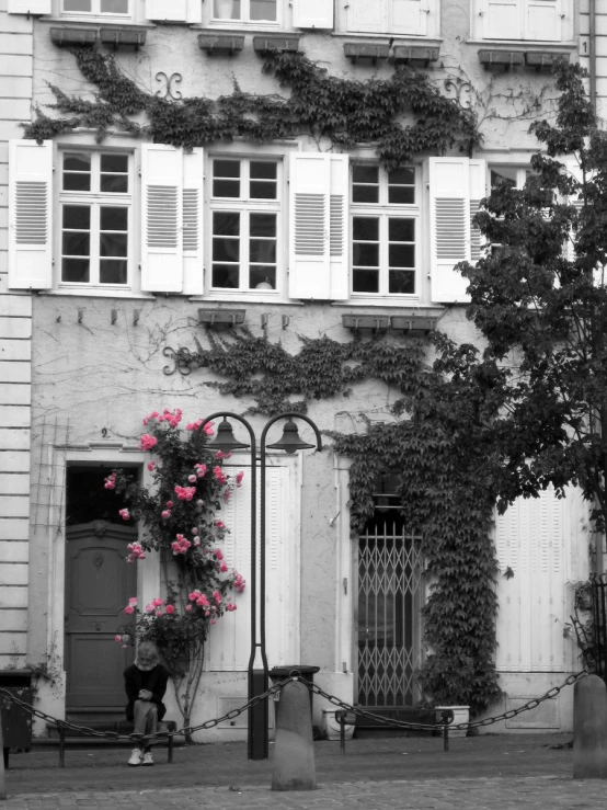 a woman sitting on the street in front of a large building with many flowers growing out of it