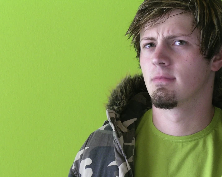 young male wearing a camouflage coat against a green wall