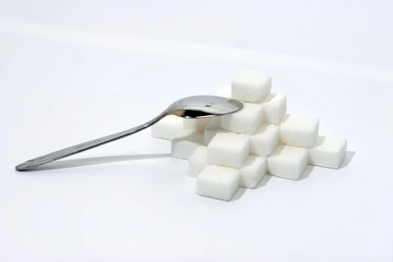 a spoon filled with sugar cubes next to some sugar cubes