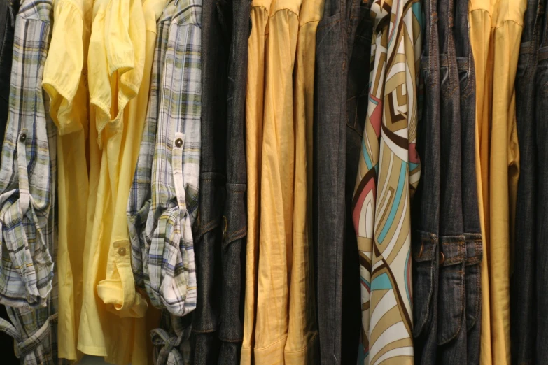 many folded ties displayed on rail with clothing hanging on wall