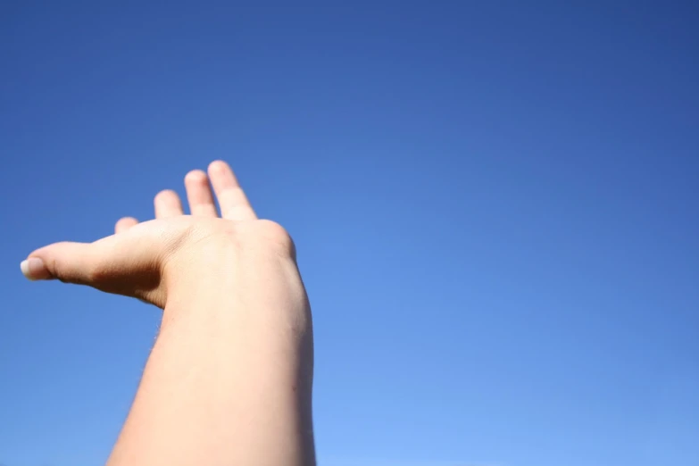 someones hand with their arm raised up on a clear day