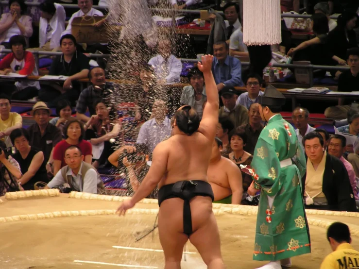 the sumo wrestler is throwing water to his opponent