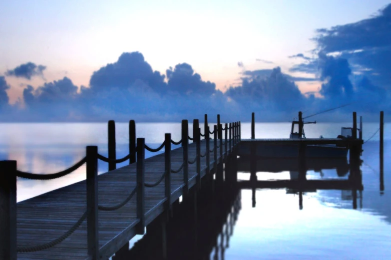 a dock with fishing equipment and ropes sticking out the water at sunset