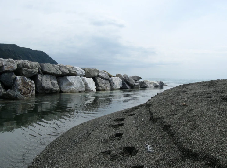 a sandy beach and shore with rocks near water