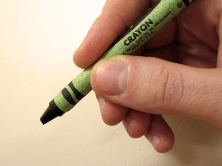 a hand holding a green crayon marker