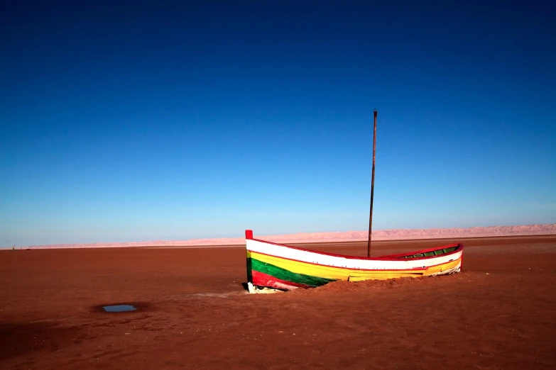 a striped boat rests on its side in the desert