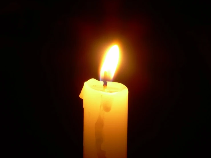 a yellow candle burning on the side of a black background
