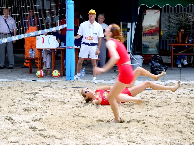 two female beach volley players are on a beach as an official watches